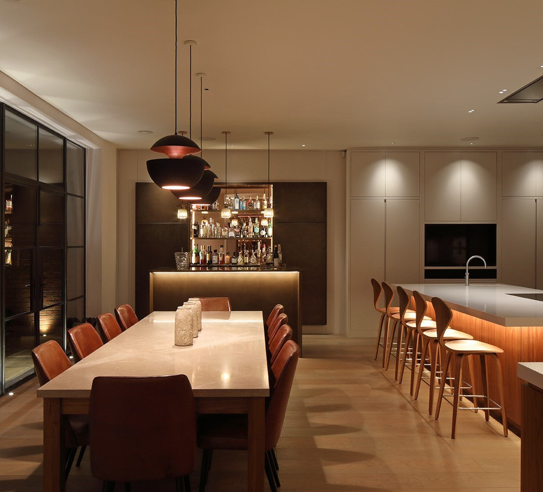 A modern living room with layered lighting—soft overhead lights, LED strip accents under shelving, and a sleek desk lamp on a side table, all glowing in harmony.